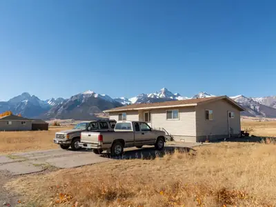 A pickup truck and an SUV parked in front of a house with the Rocky Mountains on the horizon.