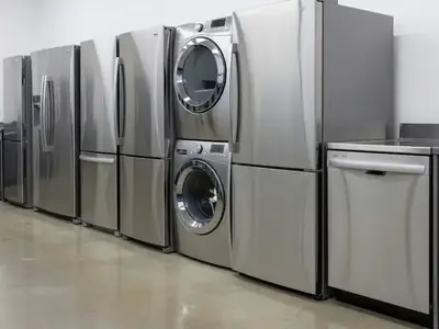 A row of new stainless steel refrigerators, a washer and dryer pair and a dishwasher on an appliance store floor, illustrating when to buy appliances in Canada: Black Friday vs Boxing Day.