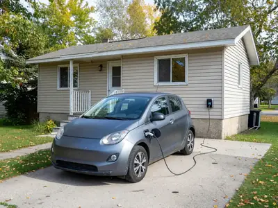 A compact electric car plugged into a charger in a home driveway.