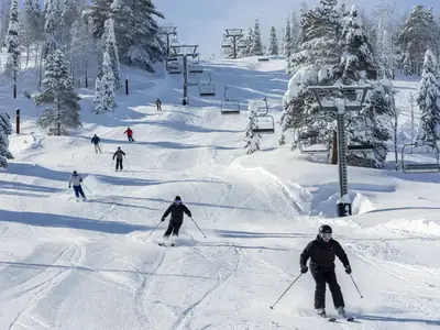 A ski hill with skiers on groomed runs and a chairlift on a sunny winter day.