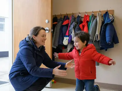 A mother picking up her preschooler from a daycare door, the child running into her arms.
