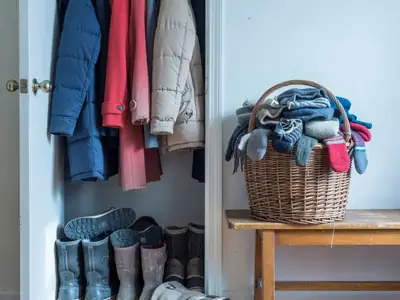 A family's front hall closet with winter coats, boots and a basket of hats and mitts.