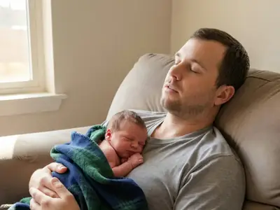 A father holding his newborn on his chest on a sofa, eyes closed.