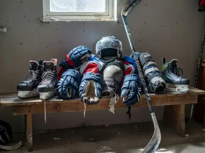 A pile of kids' hockey gear, skates and a stick drying in a garage.