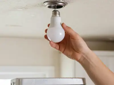 A hand screwing a new LED bulb into a ceiling fixture.