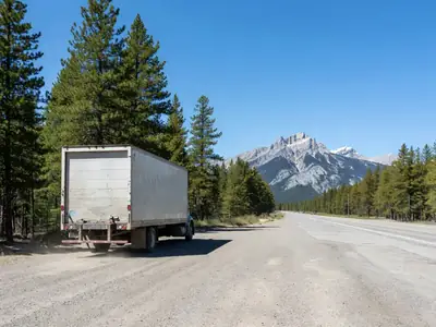 A loaded moving truck parked at a highway rest stop with mountains in the distance.