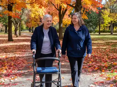 An older woman walking with a rollator walker on a park path with her daughter.