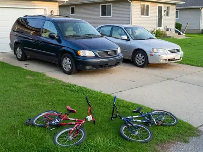 Two cars, a minivan and a small sedan, parked in a family driveway in front of a house.