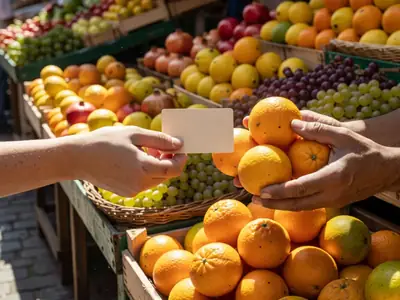 A hand paying with a plain card at a market stall abroad, the vendor handing over oranges.