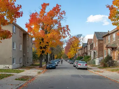 A residential street with a low-rise rental apartment building on one side and a row of brick semi-detached houses on the other.