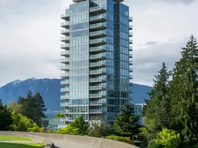 A glass condo tower with balconies and mountains behind it.