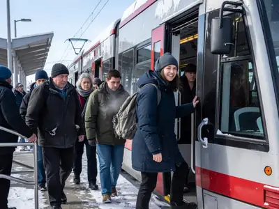 Commuters boarding a light rail train on a snowy platform.