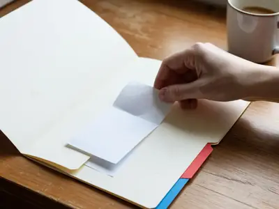 A hand placing a plain receipt into a folder labelled only with a coloured tab.