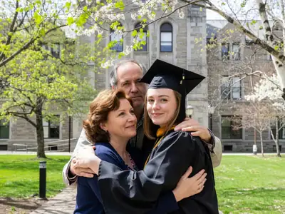 A recent graduate in a cap and gown hugging her parents outside a convocation hall.