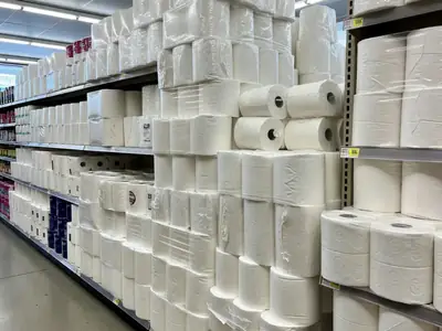 Bulk packs of toilet paper and paper towels stacked in a supermarket aisle.