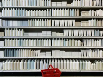 A drugstore beauty and household aisle with neatly faced shelves of plain bottles, boxes and toiletries.